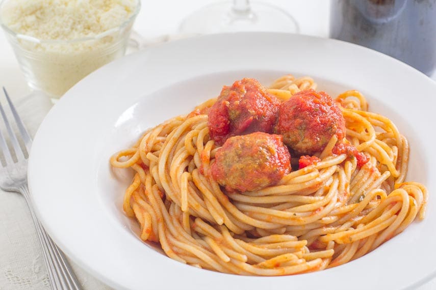 spaghetti & meatballs in a white bowl with Parmesan cheese in a small bowl in the background