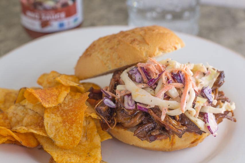 BBQ brisket topped with slaw on a roll with BBQ potato chips alongside