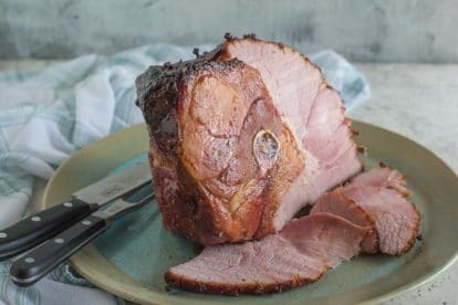 Brown sugar baked ham on a rustic platter, partially sliced