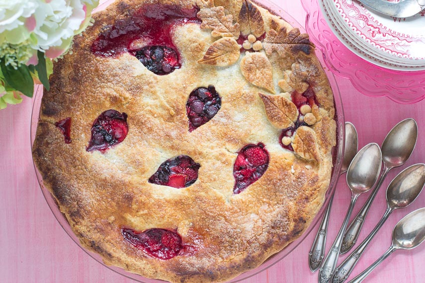 Overhead shot of berries pie, on a pink background, with decorative cut-outs in crust