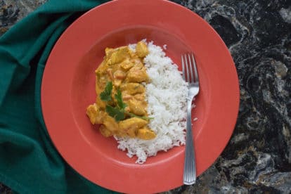 butter chicken with basmati rice in an orange bowl against a black quartz backdrop