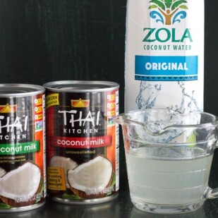 canned coconut milk and carton of coconut water against a dark background