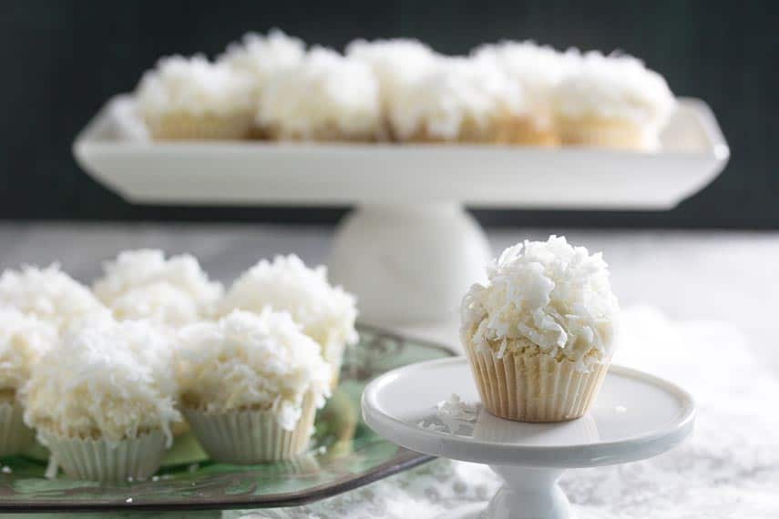mini coconut cupcakes on a platter in the background, one in the foreground on a tiny white pedestal