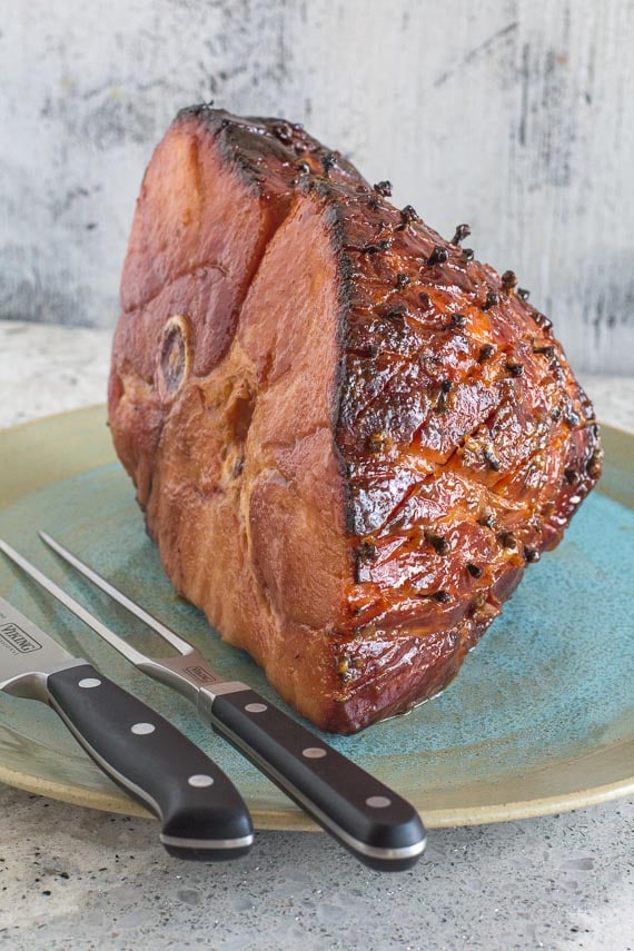 glazed baked ham on a platter with carving tools