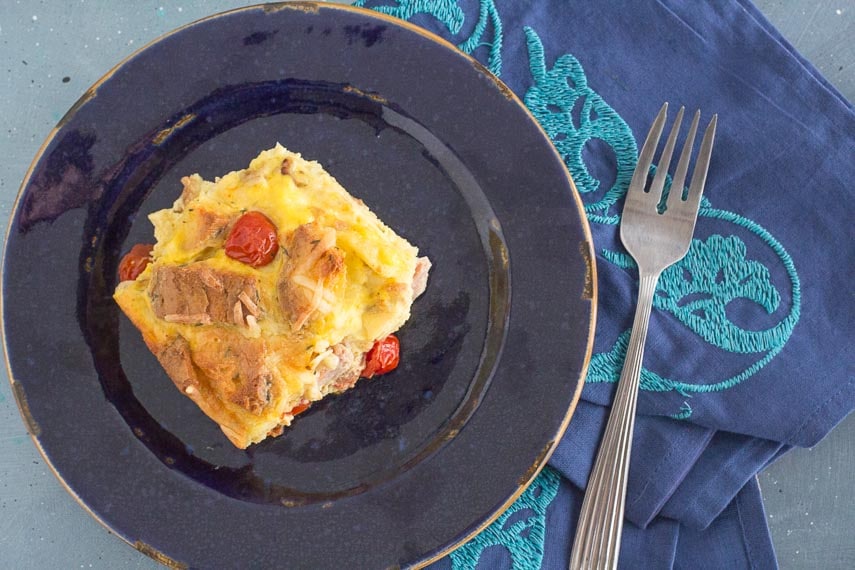 ham and egg strata on a blue plate with an embroidered blue napkin alongside
