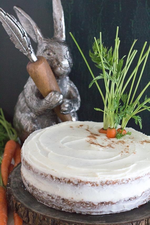 low FODMAP carrot cake with cream cheese frosting on a wooden plate with decorative bunny in the background