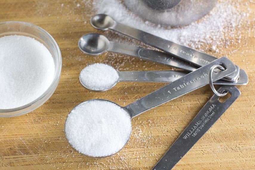 measuring white sugar with calibrated spoons against a wooden board