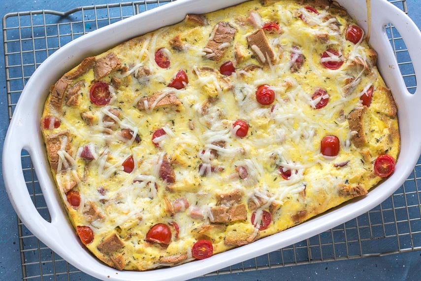 overhead shot of ham and cheese strata in a white casserole dish on a rack against a blue background