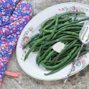 perfect steamed green beans on an oval platter with a pat of melting butter