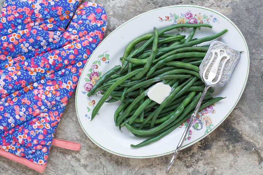 perfect steamed green beans on an oval platter with a pat of melting butter