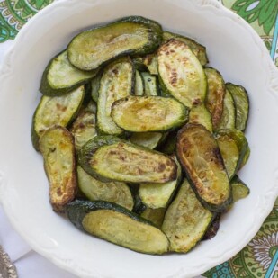 roasted zucchini slices on a white bowl with a silver spoon alongside