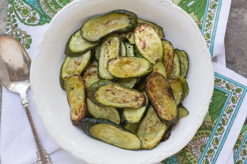 roasted zucchini slices on a white bowl with a silver spoon alongside