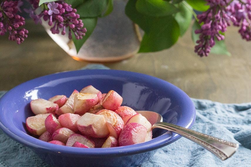 sauteed radishes in a blue bowl; lilacs in the background