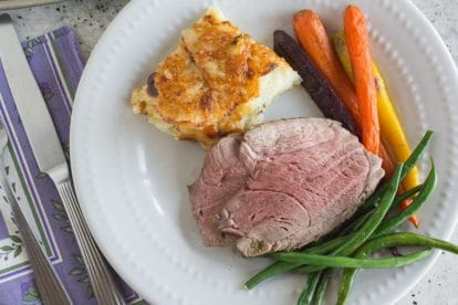 sliced leg of lamb on a plate with roasted carrots and steamed green beans