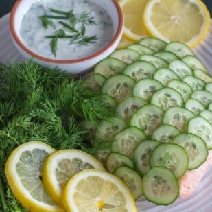 Poached salmon with cucumber scales and creamy yogurt dill sauce on a white plate