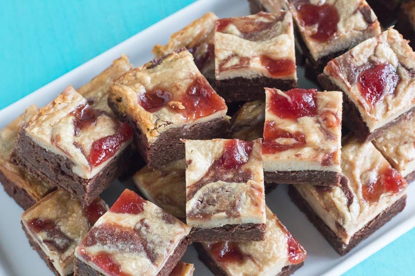 Small squares of PB & J Cream Cheese brownies on a white platter against a turquoise background