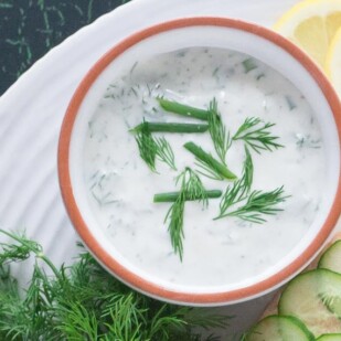Yogurt dill sauce in small white bowl with fresh dill and chives