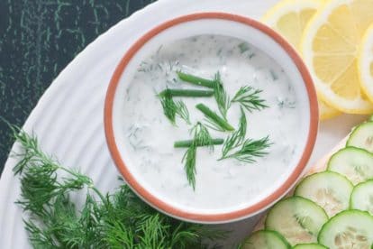 Yogurt dill sauce in small white bowl with fresh dill and chives