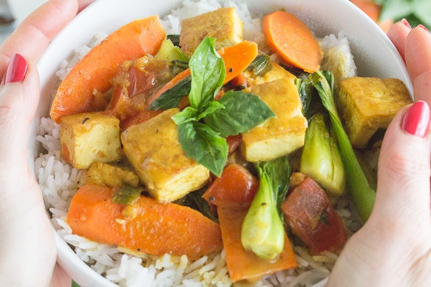 coconut tofu curry in white bowl with basmati rice, held by a women's hands