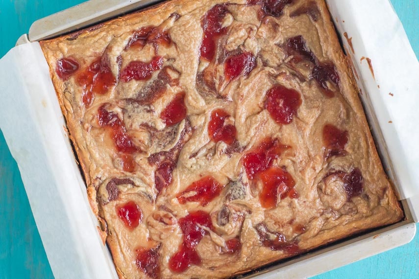 overhead image of PB & J Cream Cheese brownies in square pan against turquoise background