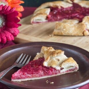 rhubarb raspberry crostata slice on a brown plate with Gerbera daisies in background