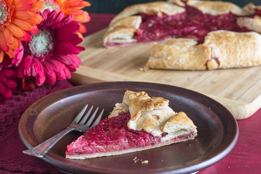 rhubarb raspberry crostata slice on a brown plate with Gerbera daisies in background