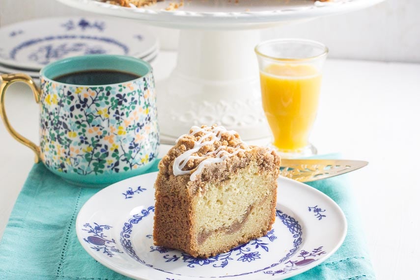 slice of cinnamon streusel coffee cake on a blue and white plate with a glass of orange juice in the background