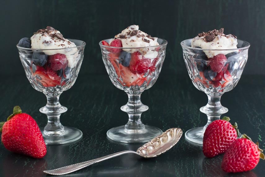 3 glass goblets holding cannoli cream on mixed berries against a dark background