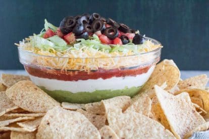 7 layer dip in glass bowl with corn chips in foreground