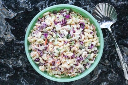 Macaroni slaw in a green bowl on a black quartz background with spoon alongside