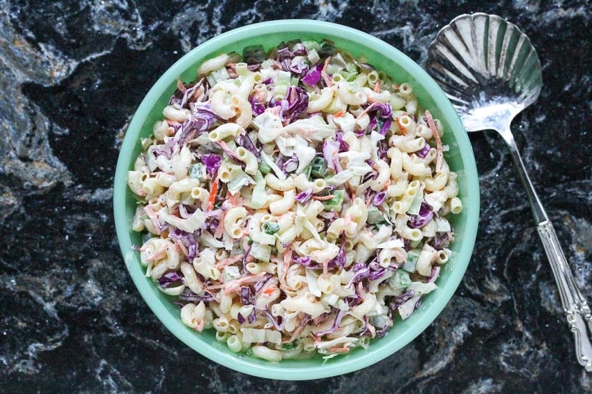 Macaroni slaw in a green bowl on a black quartz background with spoon alongside