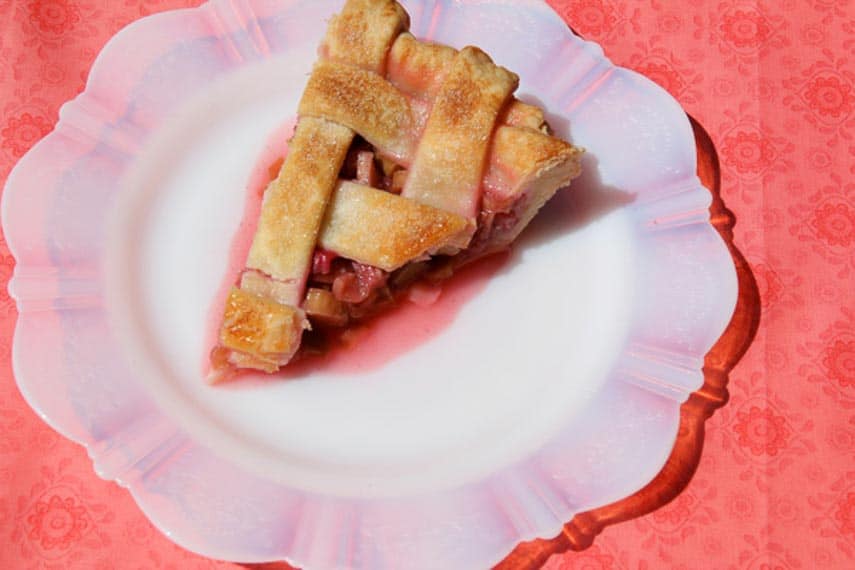 Rhubarb-pie-slice on fluted white plate on rhubarb pink floral cloth from our Rhubarb Pie with Lattice Crust recipe 
