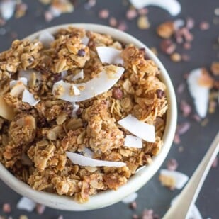 chocolate coconut granola closeup in white bowl with spoon alongside; soft focus background