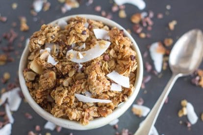 chocolate coconut granola closeup in white bowl with spoon alongside; soft focus background