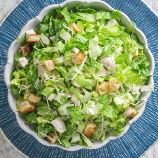 chopped chicken Caesar salad in white serving bowl on round blue placemat