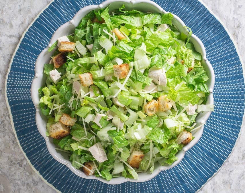 chopped chicken Caesar salad in white serving bowl on round blue placemat