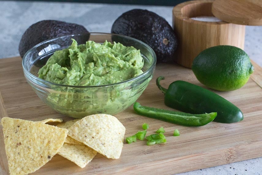 chunky low FODMAP guacamole in a glass bowl on a wooden board, chips alongside