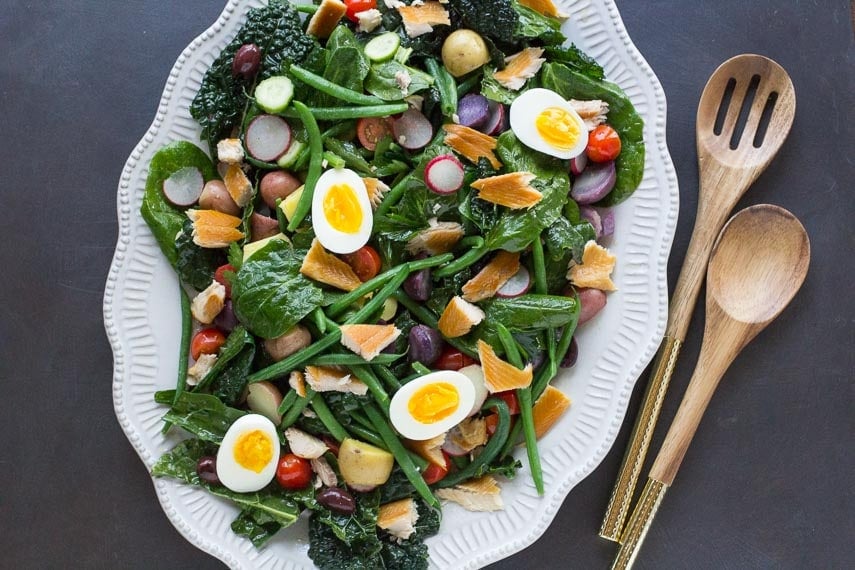 smoked trout Nicoise salad on a decorative white oval platter with wooden serving spoons