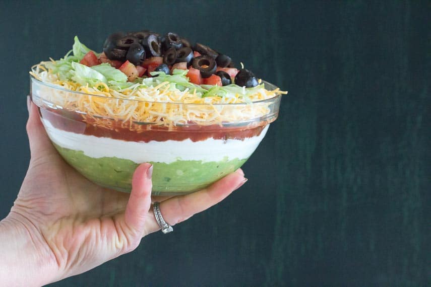 7 layer dip in glass bowl being held by a woman's hand