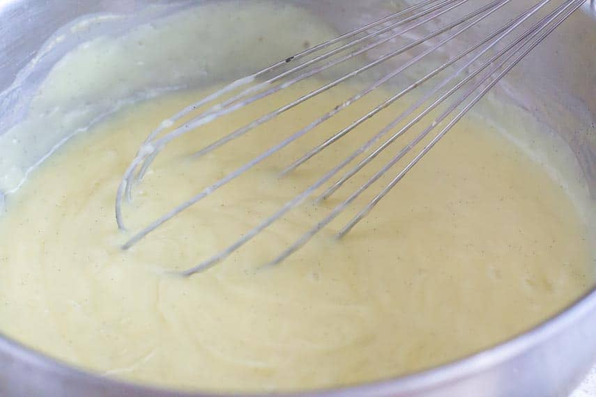 lactose-free pastry cream in pan showing vanilla bean seeds and faint whisk marks, with whisk