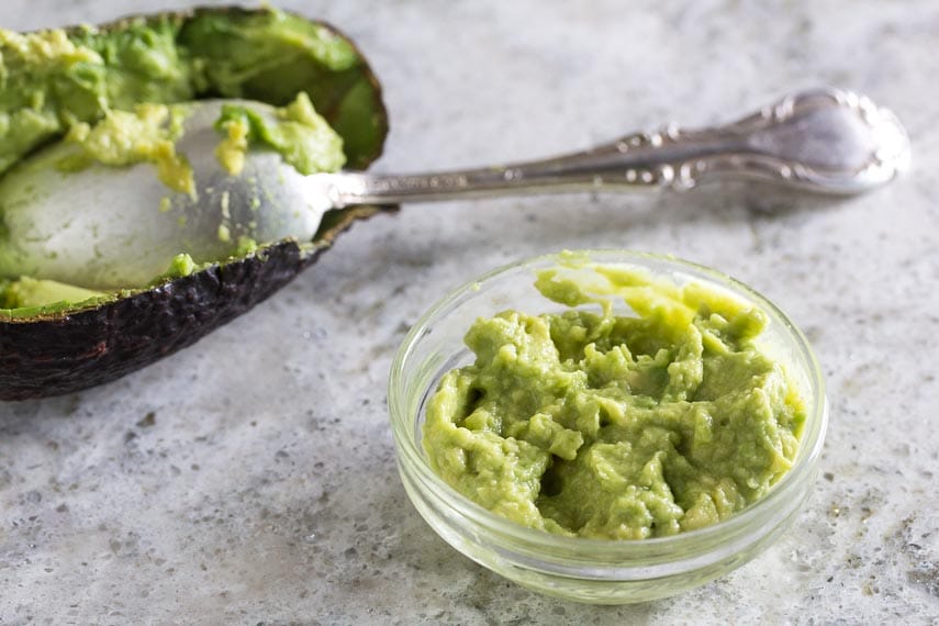 low FODMAP amount of mashed avocado (for guacamole) in small glass dish; teaspoon in background for perspective