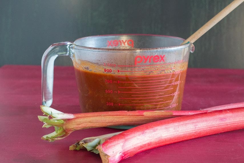rhubarb BBQ sauce in measuring cup with fresh rhubarb alongside