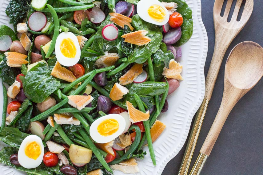 smoked trout Nicoise salad on a decorative white oval platter with wooden serving spoons