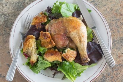 spatchcocked chicken with sourdough croutons & schmaltz on a white plate with a green salad