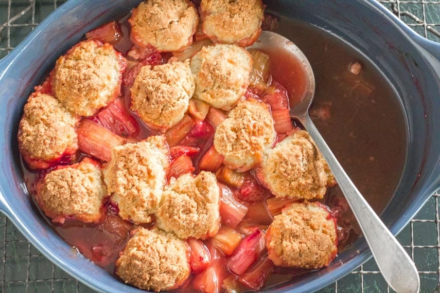 strawberry rhubarb cobbler in blue casserole with serving spoon