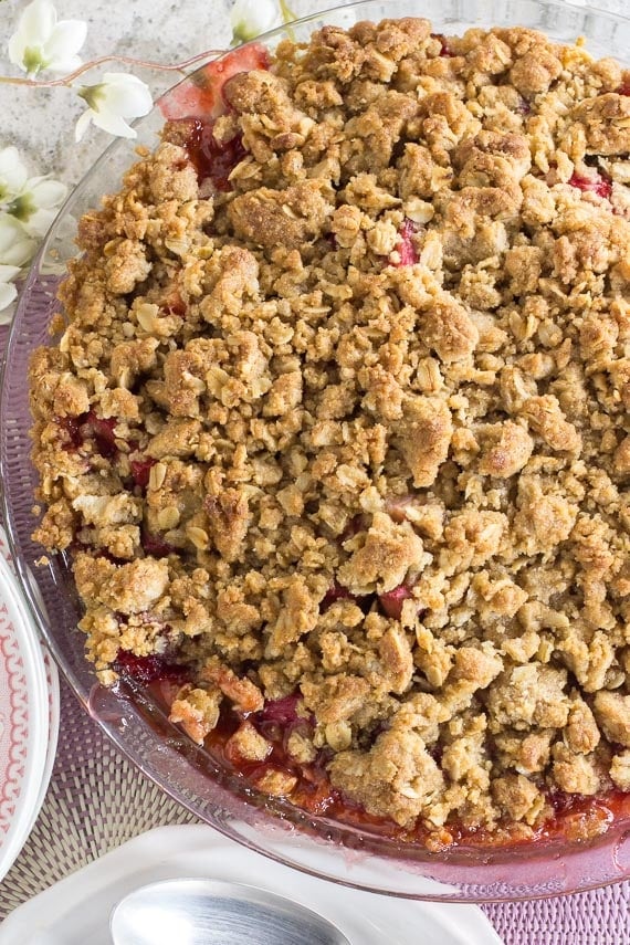 vertical image of strawberry rhubarb crisp in a clear glass pie plate