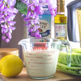 Caesar salad dressing in measuring cup with ingredients in background