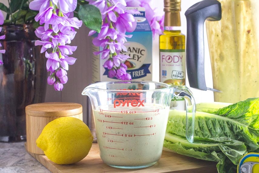 Caesar salad dressing in measuring cup with ingredients in background