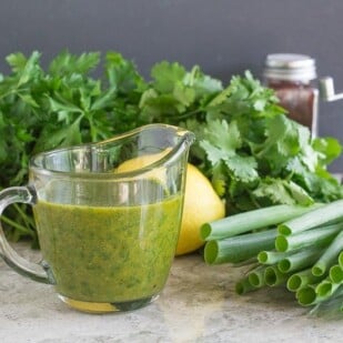 Charmoula Sauce in clear glass pitcher with ingredients in background