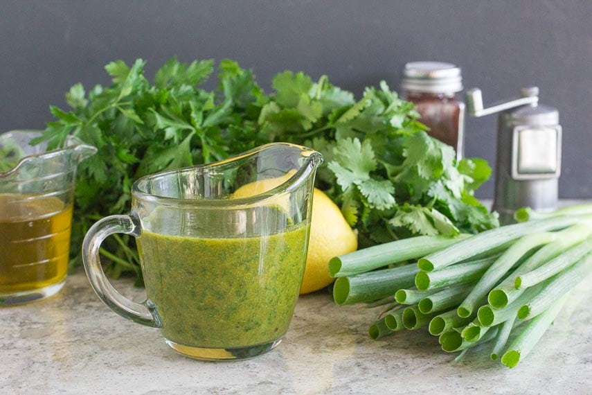 Charmoula Sauce in clear glass pitcher with ingredients in background